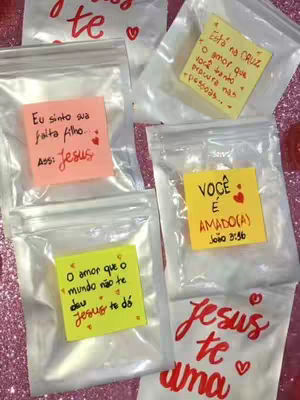 The image showcases several transparent plastic bags, each containing a folded sticky note with handwritten messages, quotes, and references to Jesus. The bags are arranged on a surface covered with pink glitter.