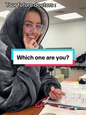 A young woman wearing large glasses and a hooded blanket smiles while looking at the camera. A text overlay reads "Which one are you?" in a box. The background has office-like elements with a desk and papers visible.