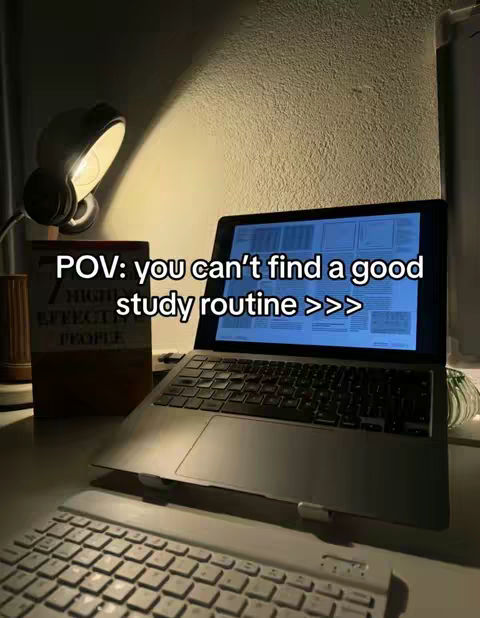 A dimly lit desk scene with a laptop, a desk lamp, a book, and a keyboard. The laptop screen displays text, there's a book and lamp on it. A keyboard is in the foreground. A warm, ambient light source illuminates the scene, creating shadows and low contrast.