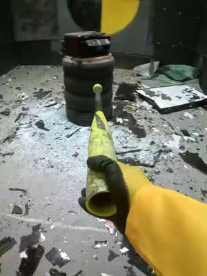The image features a first-person perspective of someone about to hit a stack of tires with what appears to be a yellow bat. The background shows a damaged area, with scattered debris and a partially visible yellow and black circle. The scene is dimly lit, giving the picture a feel of a work area or industrial space.