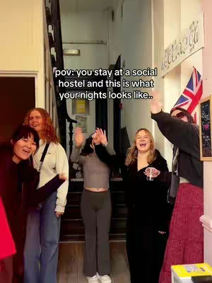 A group of young people are in a hallway or entryway. The lighting is bright, and colors are natural. The group has a wide range of skin tones and they are raising their arms up in the air, several look happy and excited smiling