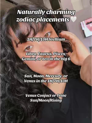 A selfie style image featuring a young woman. She has dark, wavy hair and is positioned slightly off-center, with her right hand near her face. Text overlays describe various zodiac placements. The background is blurred, but appears to be an indoor setting.