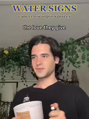 A man with dark hair is holding a candle and a spray bottle, with text overlays. The man is wearing a black shirt and looking to the side, with a background of plants and decorations. Text overlays include "WATER SIGNS" and "cancer • scorpio • pisces".