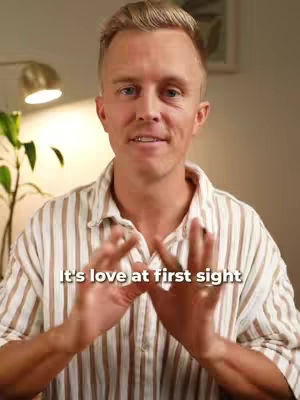 A man with blond hair, wearing a striped shirt, is smiling and gesturing with his hands. White text is overlaid at the bottom of the screen.