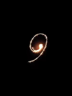 A close-up shot of a glowing number nine created with light trails on a black background. The number is in the shape of a cursive nine, with the bright light at the base of the loop. The background is solid black, creating a high-contrast, eye-catching image.