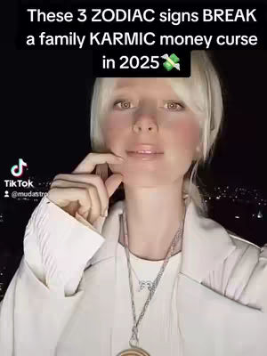 A woman with blonde hair and light skin is centered in the frame of a vertical video. She wears a white jacket and a silver necklace. Text overlays the image, with the TikTok logo and username visible in the bottom left and text at the top of the image. The background has a dark, blurred appearance with some points of light.