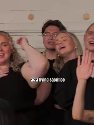 The cover image depicts a group of four individuals, seemingly captured mid-song. The individuals are diverse in their features and attire, with no central focus. The background is plain, and the lighting appears natural.