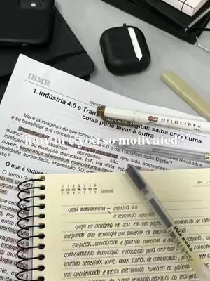 A desk covered in study materials and stationary. A sheet of paper is visible with text writing in the background. There's a notebook, pens, highlighter, and AirPods case.