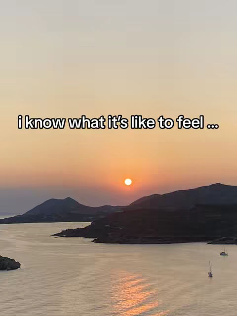 A scenic shot of a sunset over a body of water, likely a bay or lake. The sun is low on the horizon, appearing as a bright orb. Silhouetted mountains or hills are visible in the distance. The water creates a shimmering effect, and the whole scene is bathed in warm, golden light from the setting sun. A text overlay appears at the bottom.