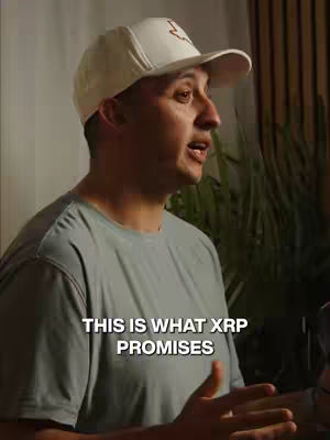A man wearing a white baseball cap and a gray t-shirt is speaking with a slight smile, a floral backdrop on the right.