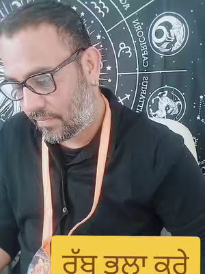 A medium shot features a man with glasses, a beard, and short hair looking down. He wears a black shirt and has a lanyard around his neck. Behind him, a black tapestry displays astrological symbols. The bottom is a yellow rectangle with text in a foreign language.