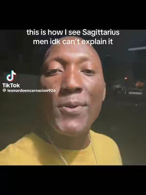 A close-up shot of a Black man looking directly at the camera. He is wearing a yellow shirt. Above him, the text overlay says 'this is how I see Sagittarius men idk can't explain it'. The TikTok logo is in the top-left corner, and his username is displayed below it.