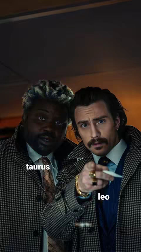 The cover image shows two men side-by-side, presented head and shoulders within a darker, slightly blurred setting. The man on the left has short, textured dyed blond hair and is wearing glasses, a white collared shirt, and checkered coat. The man on the right has dark, slicked-back hair, a trimmed mustache, and is pointing a finger towards the viewer adding a light color. Text overlays identify them as "taurus" and "leo".