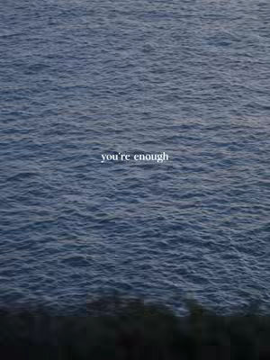 An image of a body of water. The water appears to be a deep blue with some texture, suggesting waves or ripples. The text "you're enough" is horizontally centered in white, appearing on the surface of the water, while the lower portion of the image is a dark, shadowed area, which could be the shoreline or the bottom of the body of water.