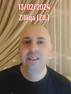 A man with a shaved head is centered in the frame, smiling slightly at the camera. The background features a curtain and soft lighting. Text overlays at the top indicate a date and the cryptocurrency Zilliqa.