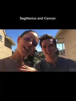 Two individuals, a woman and a man, are captured in a selfie-style shot, seemingly in an outdoor setting with a backdrop of buildings and a clear blue sky. The woman is positioned on the left, and the man is on the right. Text overlaid at the top reads "Sagittarius and Cancer:" in a clean, white font. The composition uses natural lighting, highlighting the subjects' faces.