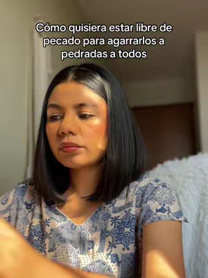 A woman with black hair and fair skin looks slightly to the side with a serene expression. Text overlays the image in the top which reads "Cómo quisiera estar libre de pecado para agarrarlos a pedradas a todos". She appears to be wearing a blue floral top. The background is out of focus.