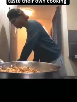 A person wearing a black cap and long sleeves is shown cooking . The person is looking down into a silver pan with food. The person is inside a building with light on.