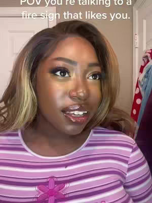 A close-up shot of a woman with a light complexion, wearing a purple and white striped shirt, looking towards the right of the frame with a slightly open mouth, as if she's speaking. The background is a soft focus, suggesting a room interior with a door and a glimpse of clothing.