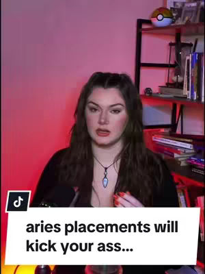 A woman with long brown hair is speaking. She's wearing a black top and necklace, seated in front of a pink-lit background with a bookshelf. Text on a white overlay reads, "aries placements will kick your ass..."