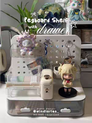 The cover image showcases a white pegboard shelf with a clear drawer. It's filled with various aesthetic desk accessories and decorative items, including figurines, post-it notes, and small trinkets. The setup is presented against an out-of-focus background with a plant and a globe visible, providing a clean and organized aesthetic.