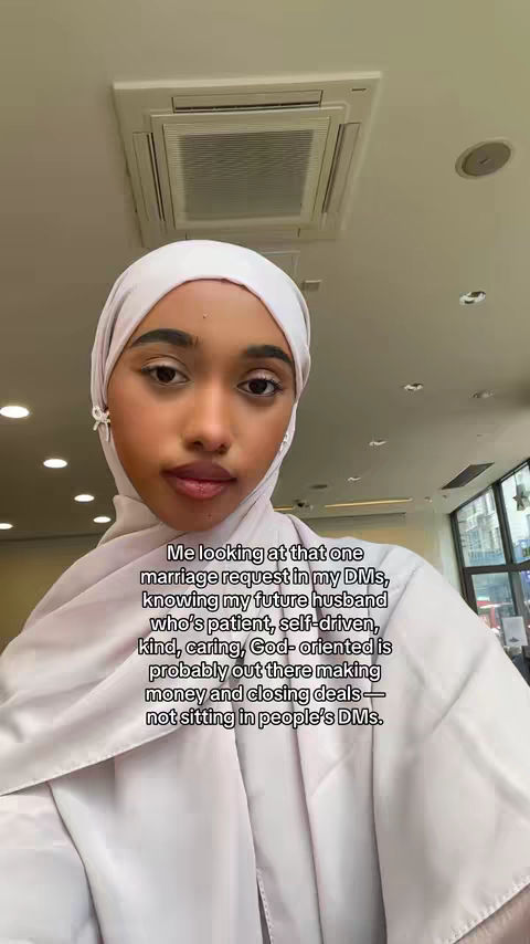 A young woman wearing a white hijab and neutral-colored clothing looks directly at the camera with a slightly inquisitive expression. The background is a plain white ceiling, punctuated by an air vent. Text overlays the image.