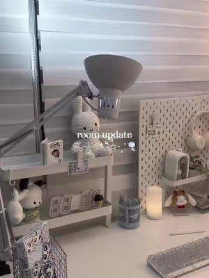 The cover image shows a well-organized desk setup with a white desk and various cute accessories. A lamp is positioned to the left and above, providing illumination. A plush bunny sits on a shelf, and other decorative items are visible, including a digital clock. The overall aesthetic gives off a clean and organized vibe. The text overlay says 'room update'.