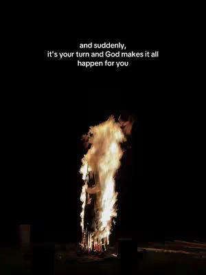 A nighttime image featuring a central bonfire with tall flames against a pitch-black background. Above the bonfire, white text reads, 'and suddenly, it's your turn and God makes it all happen for you'.