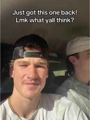 The cover image shows a selfie-style shot featuring a young man in a black trucker hat and a white shirt from the chest up. He is inside a vehicle looking towards to the camera and smiling. There is another person in the background wearing a white hat with only his ear visible. The top of the image is in black font.