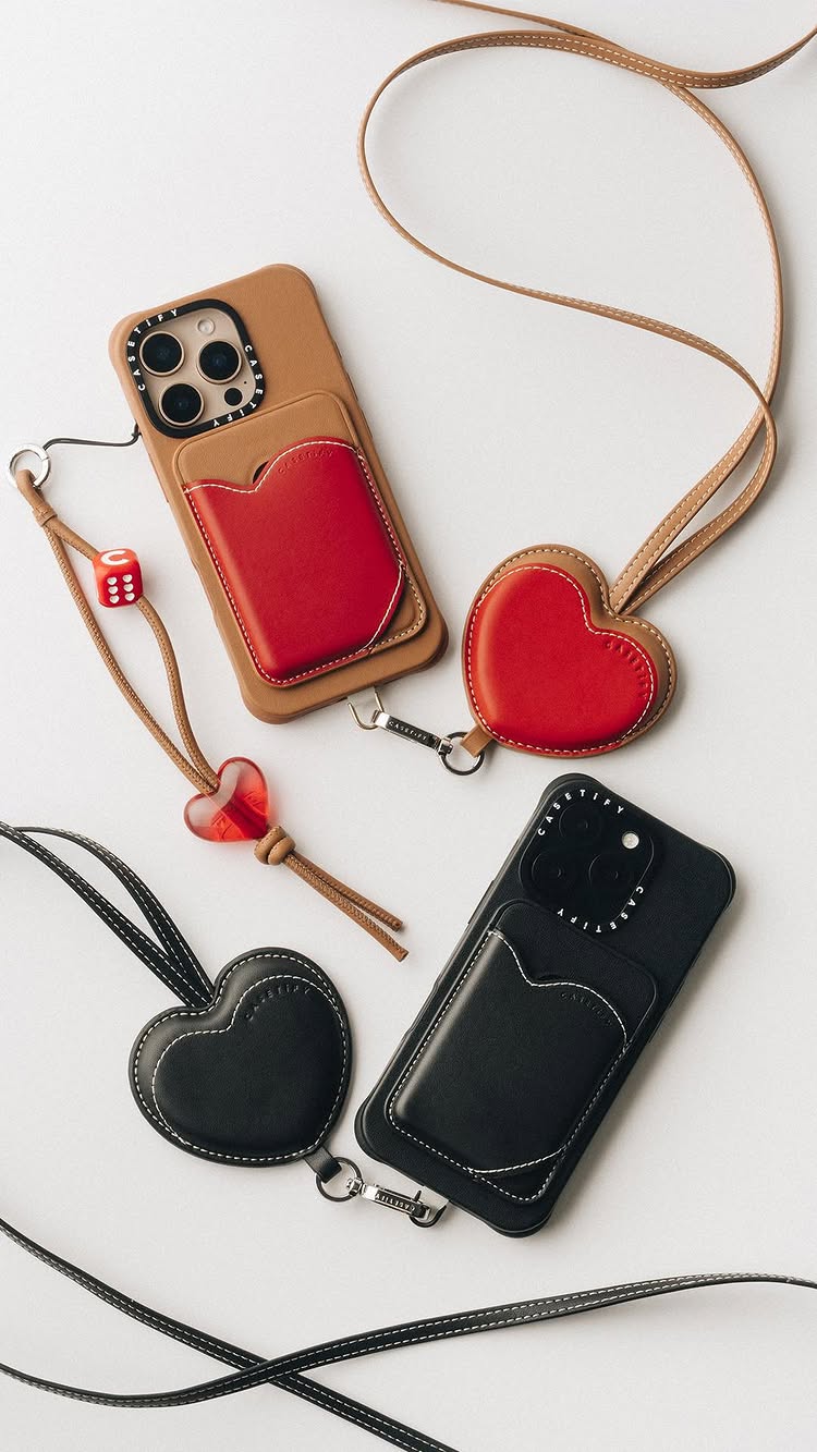 A product shot featuring two smartphones with attached heart-shaped cases and lanyards, along with detached heart-shaped accessories and a red die. The scene is set on a white background, and the items are arranged in a visually appealing manner to highlight the design and functionality.