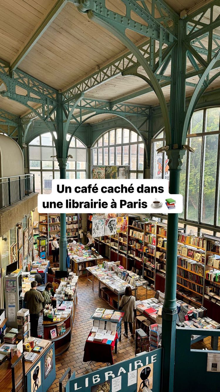 An interior shot of a library with a cafe. The focus is on the high ceilings supported by large, arched metal beams painted in a teal color. The image is well-lit, showing rows of bookshelves, tables, and patrons browsing the books in the shop. The foreground features signage advertising the cafe as a hidden gem, with text overlaying a small graphic of a coffee cup and books.