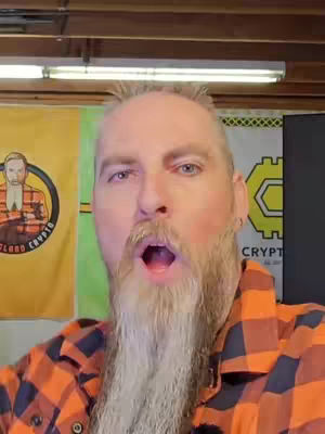 A man with a surprised expression opens his mouth, wearing a plaid shirt, with a backdrop featuring flags that have logos promoting crypto.