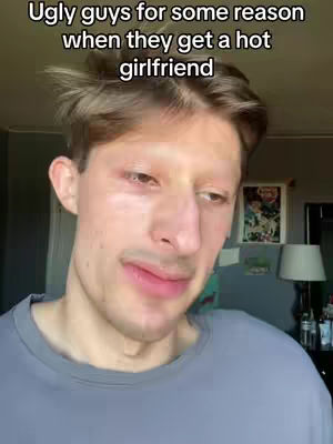 A man with light skin, short brown hair and light eyebrows is the focus of the image. He is wearing a grey t-shirt and making a slightly pained face. Above the man, the text in white reads, "Ugly guys for some reason when they get a hot girlfriend."