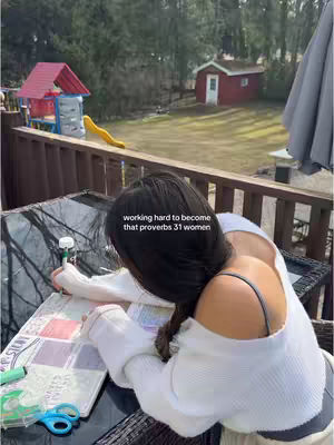 A woman is sitting at a table outside, studying. Over her shoulder, a backyard scene with a playset and small red building is visible. The text overlay reads "working hard to become that proverbs 31 women"