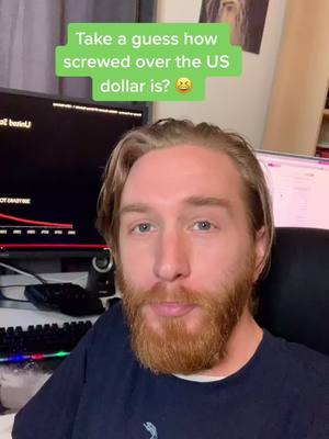 A man with a red beard is facing the camera, with text bubble overlayed above his head. Dark monitors and a keyboard are present in the background.