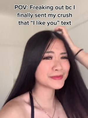 A young woman with long black hair is centered in the frame, looking towards the side with a slight smile. Text overlays read "POV: Freaking out bc I finally sent my crush that 'I like you' text". The background appears to be a plain wall.