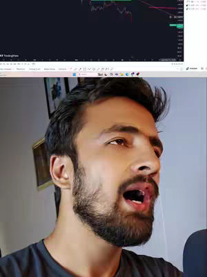 A man is captured in a selfie style, looking to the side with his mouth open as if speaking or reacting to something. Above him, a laptop screen displays a financial chart plotting what appears to be a downward trend, suggesting discussion of market performance. The background is softly lit, with hints of a room visible. The overall composition is a blend of personal expression and data analysis.