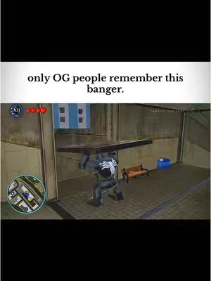 The image shows a screenshot from a Lego Marvel Super Heroes video game. The game's UI elements are visible in the corners. The main focus is on a Venom-like character lifting a large object with the game's setting in the background.