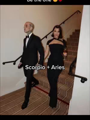 The cover image shows a couple walking down a staircase inside what appears to be a luxury building. The man is wearing a black tuxedo with a bow tie, and the woman is in a black dress. Text overlaid on the image reads "Scorpio + Aries". The background shows elegant architectural details, and the couple is holding hands.