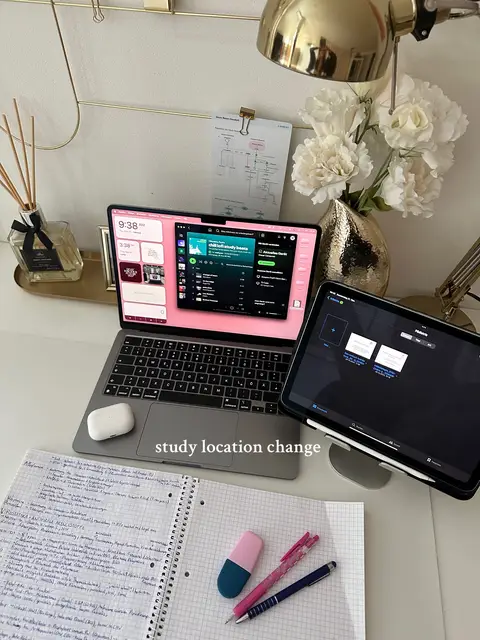 The cover image shows a well-lit desk set up for studying. A laptop is open, displaying a Spotify window with a pink themed background. An iPad is propped up to the right, also displaying a screen. A notebook with handwritten notes, an eraser, pens, and a pair of AirPods are spread across the surface along with decorative elements, such as a vase of flowers with a gold desk lamp. The text overlay reads 'study location change'.