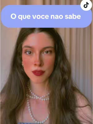 A woman with long brown hair and a pearl necklace is centered in the frame, looking directly at the camera. Above her head is a light blue banner with white text, and a TikTok logo is in the top right corner. The background is a soft, neutral color.