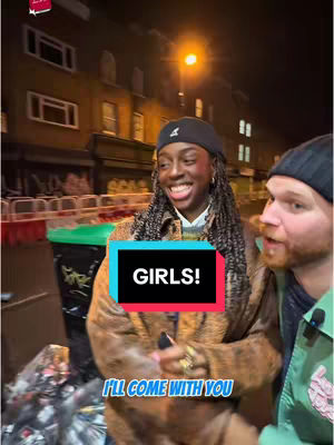 A woman with long braids wearing a black cap is smiling while standing next to a man. The setting appears to be an outdoor street at night, with buildings and a street light in the background. A text overlay is placed over the image.