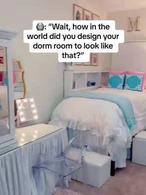 The image is a well-lit dorm room scene. Soft, natural light fills the room, hitting the details. A bed with a white ruffled comforter and pink pillows is in the background. A desk with a lighted mirror and a clear acrylic chair sit in the foreground. Text overlayed on the image reads, "Wait, how in the world did you design your dorm room to look like that?"