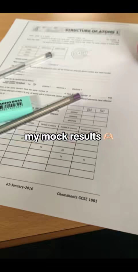 The image is a vertical shot of a desk covered in papers, a pen, and an eraser. The main element is a test paper with the header "STRUCTURE OF ATOMS". Below, there's a table with numbers, a pencil, and an eraser. The text "my mock results" is overlaid on the image. The overall composition is well-lit.