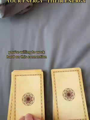 The image shows two stacks of tarot cards laid over a gray cloth. Text on top of the image reads "YOUR ENERGY - THEIR ENERGY". The foreground features cards with light brown backs and ornate borders. In the bottom middle of the image, more text reads "you're willing to work hard on this connection".