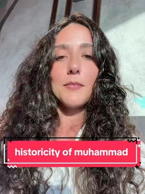 A woman with long, curly dark hair is centered in the frame, looking directly at the viewer. Behind her is a light-colored wall and a partially visible, wooden structure. A red banner with white text reading 'historicity of muhammad' is placed at the bottom of the image.