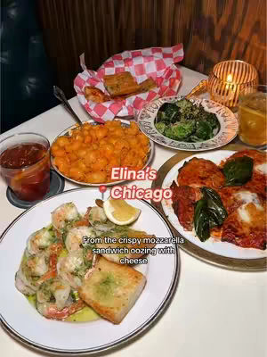A restaurant table setting with various dishes of food and drinks, including a plate of shrimp and a plate of pasta with sauce, a glass of red liquid, and a small candle in a glass holder. The overall tone is warm and inviting, with a focus on the food.
