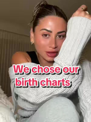 A woman with light skin and brown hair, half-up in a bun, looks toward the camera with a slightly open mouth. She is wearing a sleeveless black top under a light gray, chunky knit sweater. The text overlay on the image reads, "We chose our birth charts."