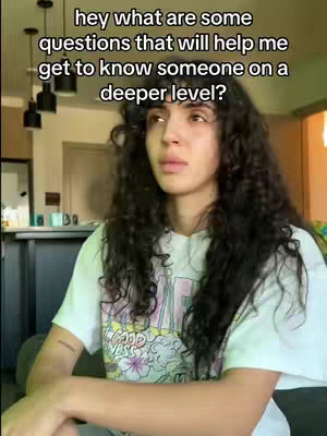 A young woman with long, curly hair and a white t-shirt is looking up and slightly to her right. The text overlay states "hey what are some questions that will help me get to know someone on a deeper level?"