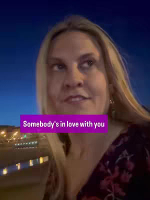 A woman with long blonde hair is looking slightly to the left. A banner with text overlaps the bottom part of the image, and the background is dark, with city lights visible. The composition is a medium shot focusing on the person's face and upper body, with a blurred background.